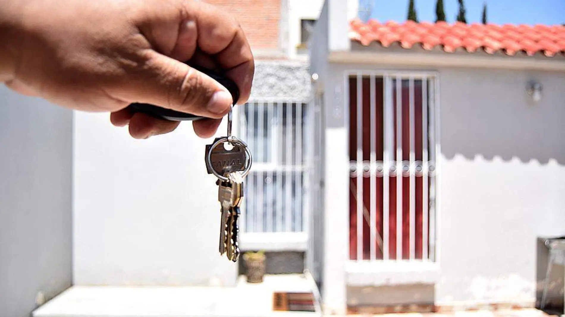 Mano sosteniendo unas llaves frente a una casa